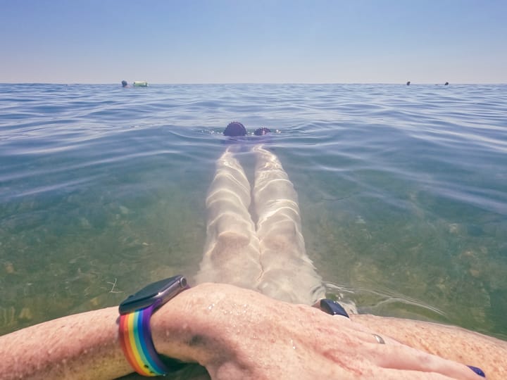 Person floating in calm water with their hands resting on a toe float looking at the horizon.