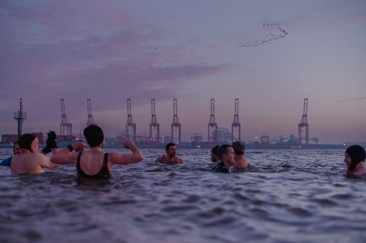 A group of people swimming in an industrial river at dawn.