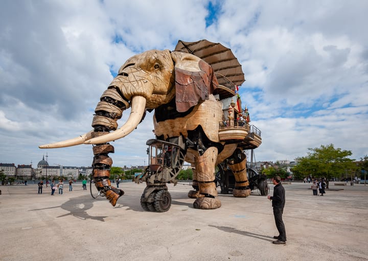 A giant elephant made from wood walks around an empty dockyard.