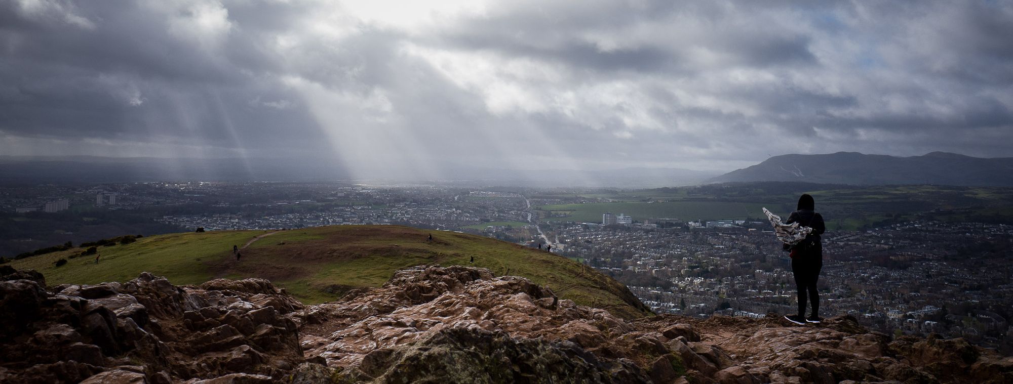 View from top of big hill in Edinburgh. A person stands to the right looking out.
