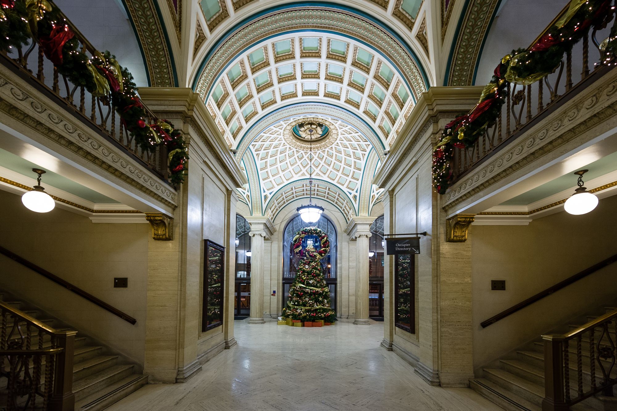 Wide angle photograph of ornate architectural entrance way covered in decorations. There is a Christmas Tree in the middle.