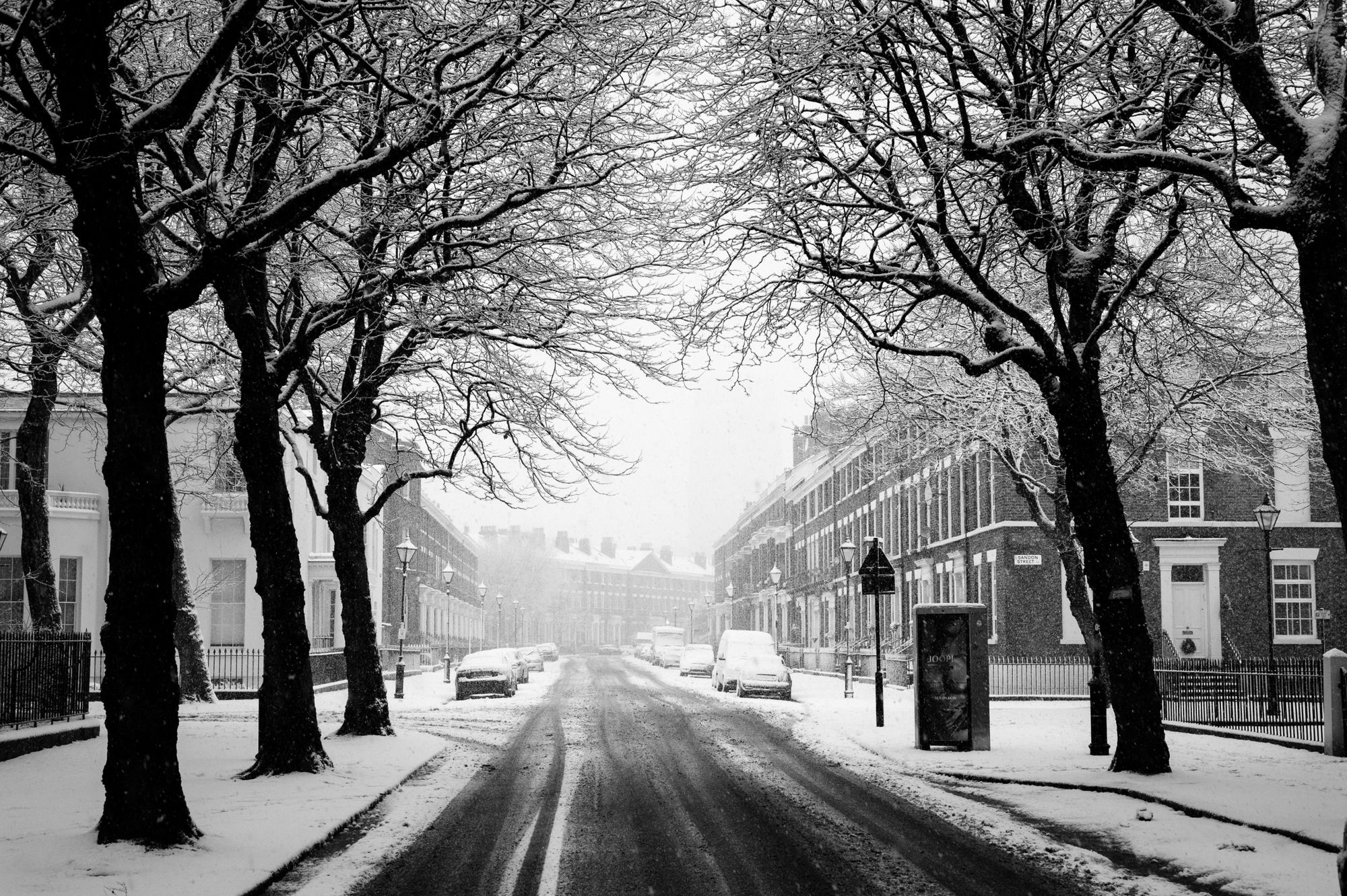 Snowy urban landscape featuring grand Victorian terraces and trees either side of the road.