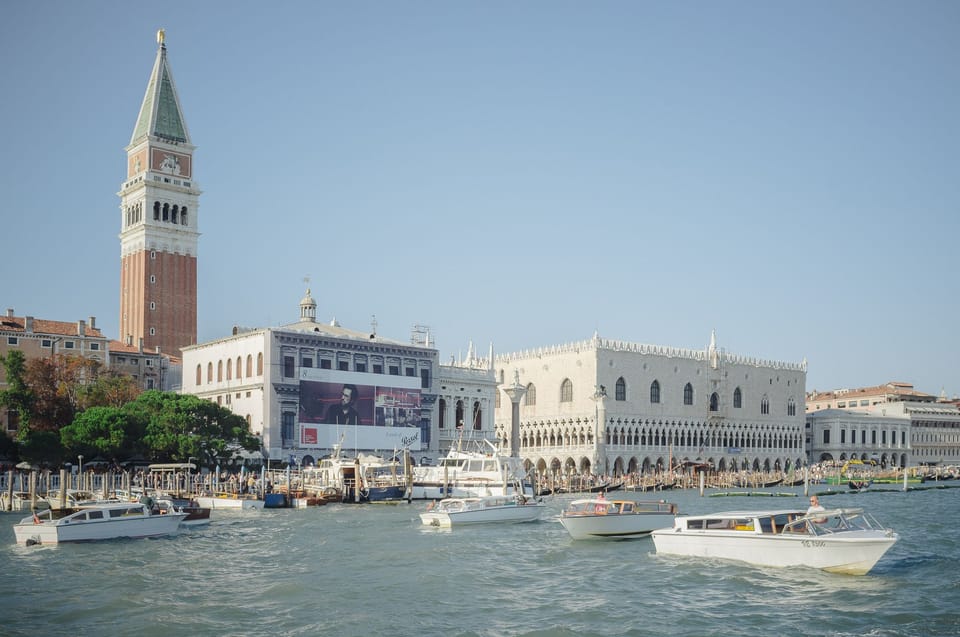 Boats passing by the main square in Venice. A large clock tower is to the left.