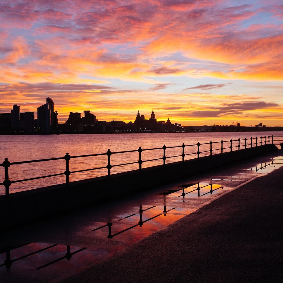 Sunrise over the River Mersey reflected in puddles of water along the promenade.